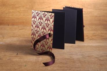 Leporello unfolded from black photo cardboard and firm book cover with red and gold Florentine paper and red ribbon